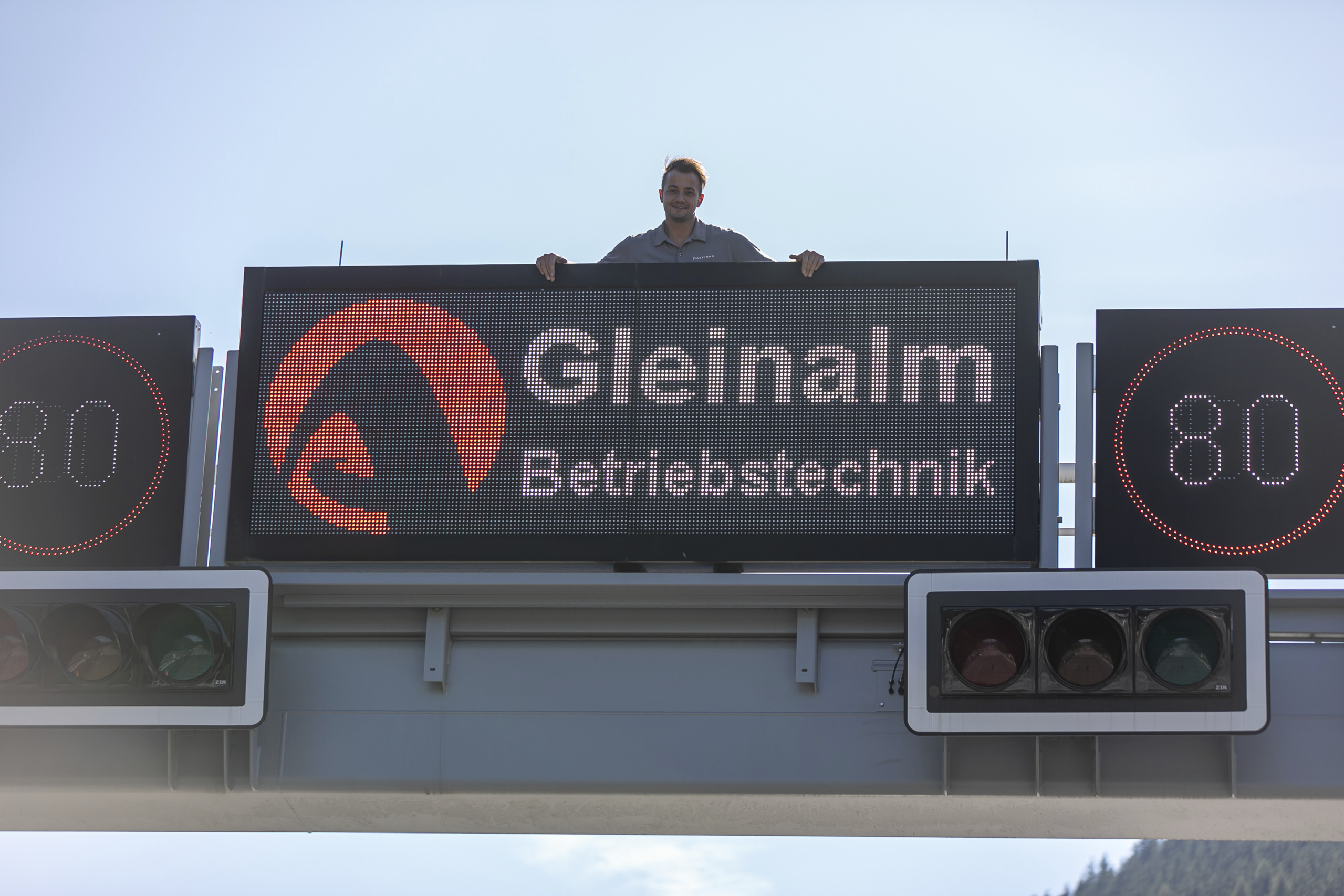 Ein Lehrling steht auf einem Überkopfhinweiser mit der Aufschrift "Gleinalm Betriebstechnik"