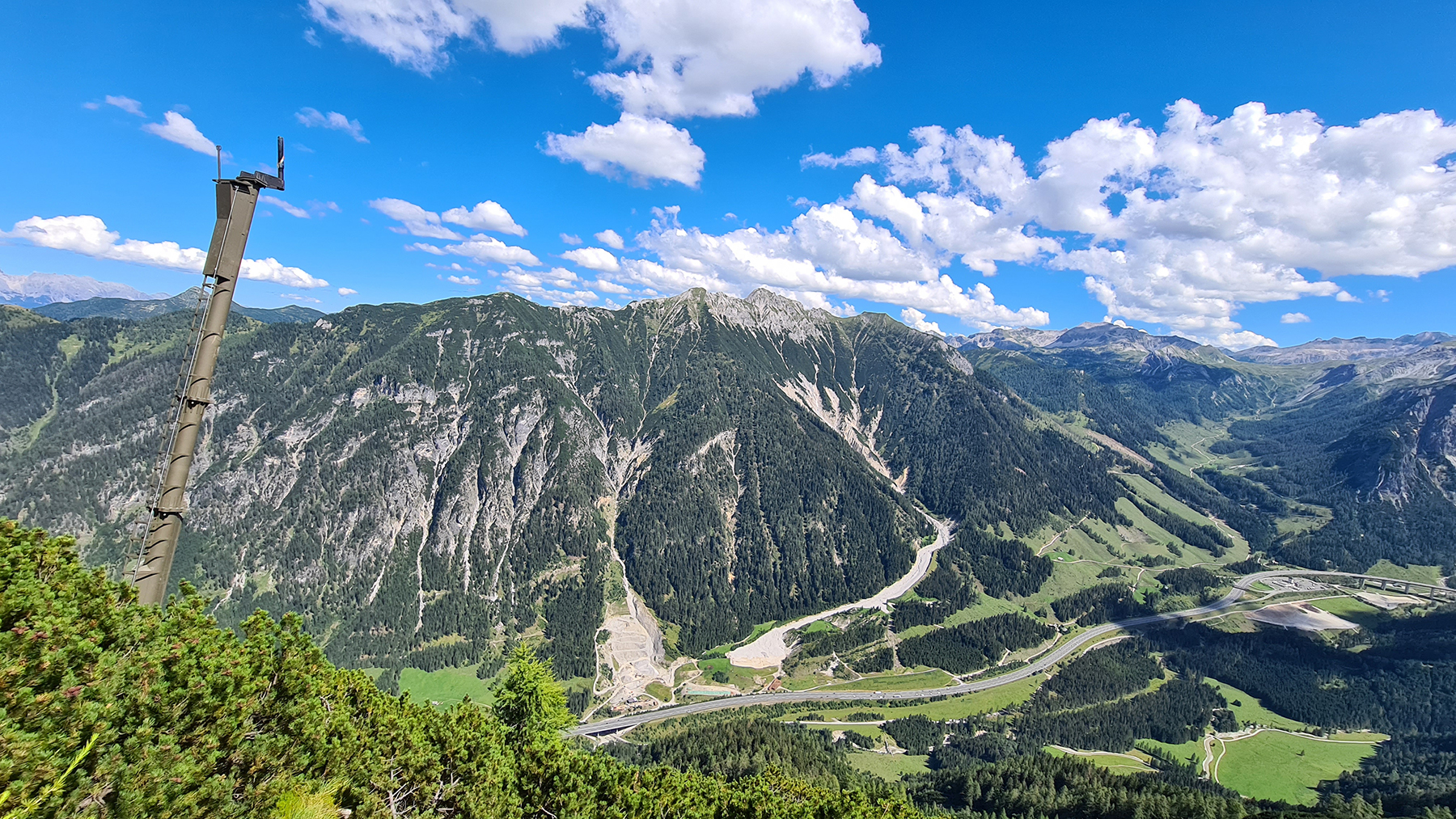 Blick von einem Abhang auf eine Autobahn. Ein Lawinensprengmast ist im Bild.