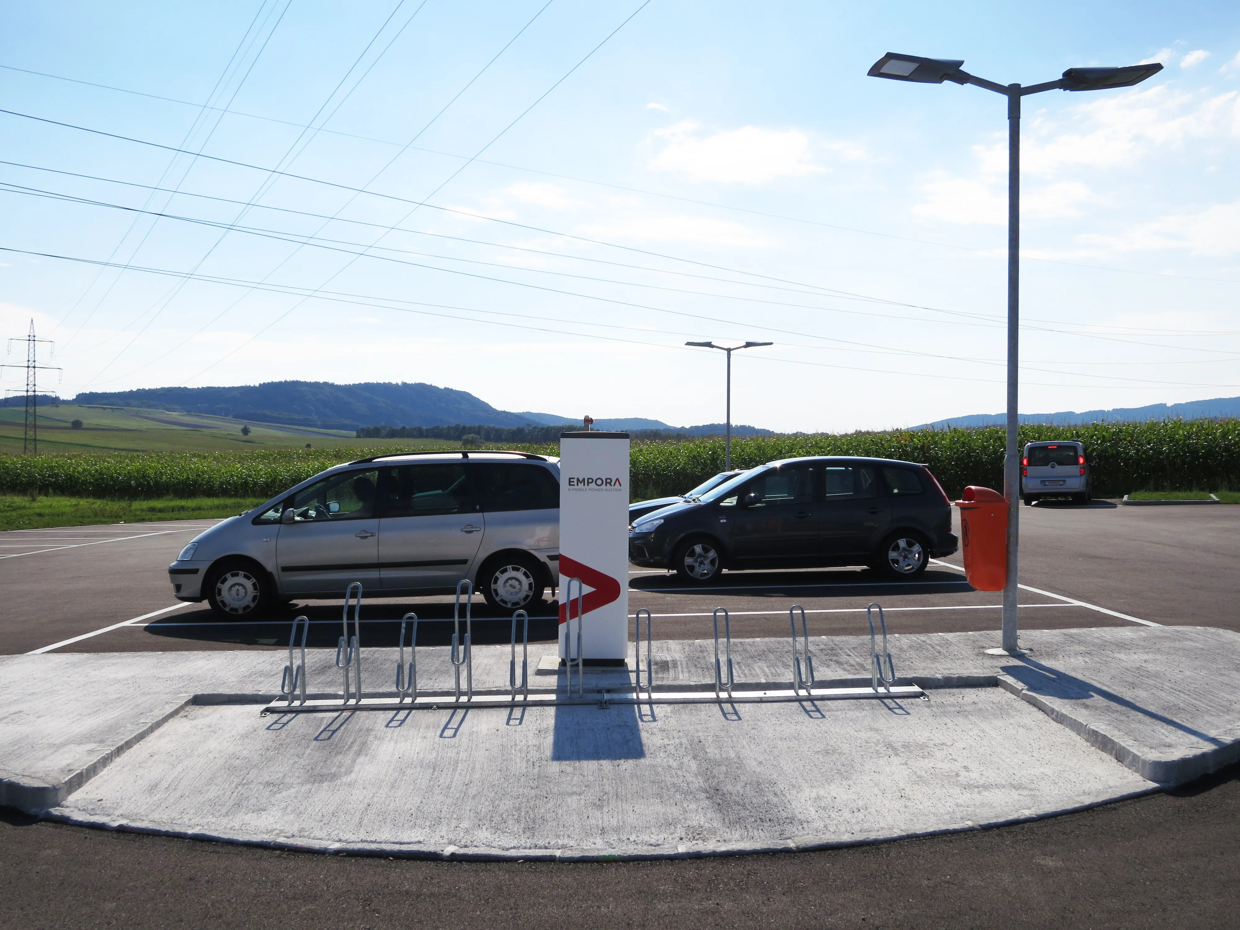 Abgestellte Fahrzeuge auf einem Park and Drive Platz mit E-Ladestation und Fahrradsständern  im Vordergrund