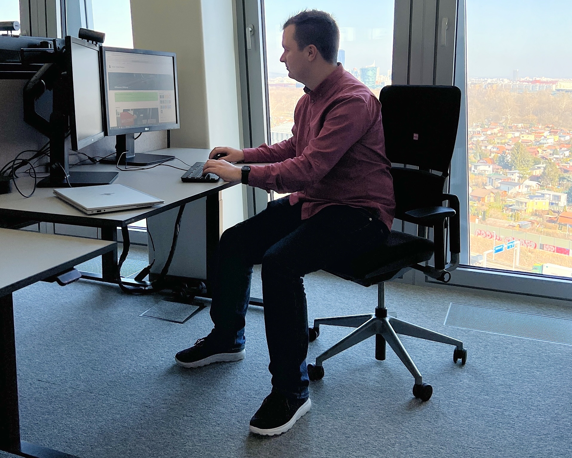 Ein junger Mann sitzt an einem Schreibtisch vor einem Computer und lächelt in die Kamera