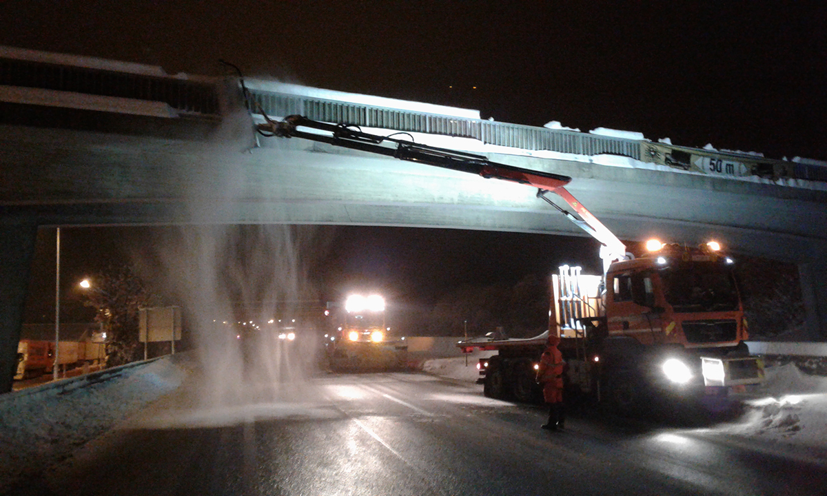Lkw mit Kran bürstet Schnee von einer Brücke bei Nacht
